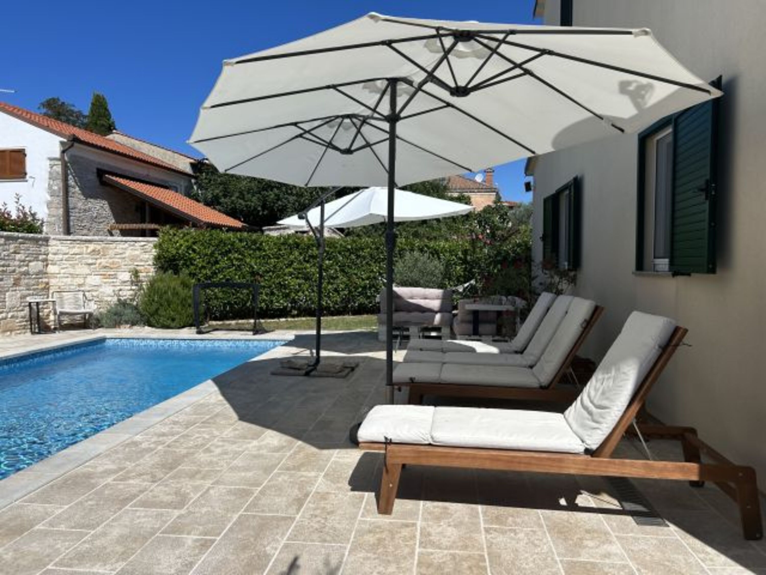 Blick auf die großzügige Poolterrasse mit Liegestühle und Sonnenschirmen